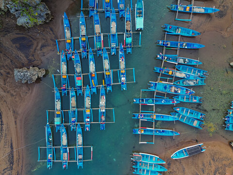 Aerial view of blue outrigger fishing boats moored in the clear turquoise waters of Baron Beach in Yogyakarta, Special Region of Yog, Indonesia.