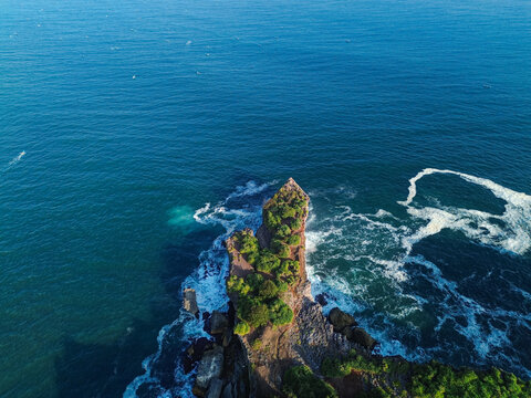 Aerial view of Baron Beach featuring a rocky headland with lush greenery surrounded by blue ocean and white sea foam in Yogyakarta, Special Region of Yogyakarta, Indonesia.