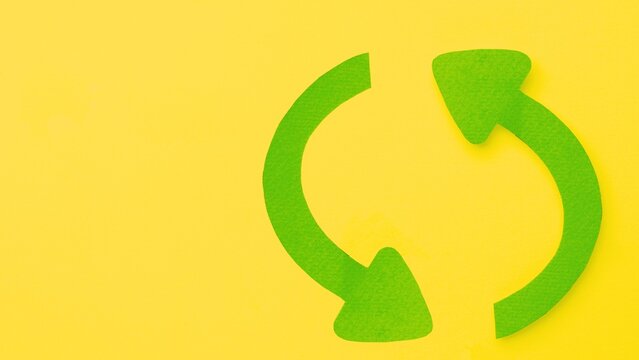 Green circular arrow symbol made of paper texture on bright yellow surface