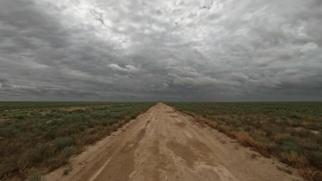 Driving on a dirt road through a vast landscape under cloudy skies
