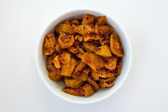 Delicious homemade amra achar or hog plum pickle served in white ceramic bowl on white background. Traditional South Asian spicy sweet condiment for meals. Top view.