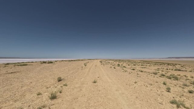 Driving through arid landscape with dirt road and sparse vegetation visible