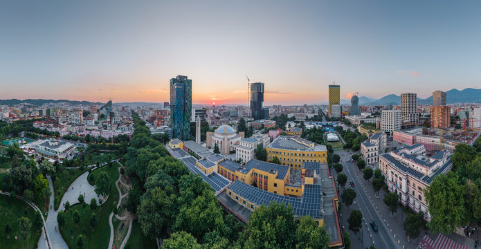 Aerial view of the city center of Tirana at sunset, featuring modern skyscrapers, the historic Et'hem Bey Mosque, lush green parks, and urban architecture in Tirane, Tirana County, Albania.