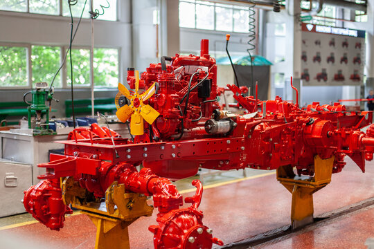 Red tractor chassis under assembly on factory assembly line. Mechanical engineering, heavy machinery production, modern farming equipment development.