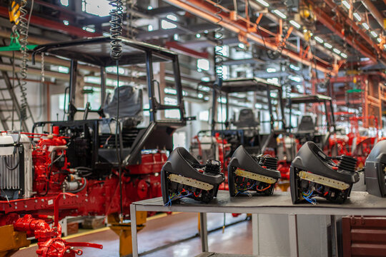 Tractor assembly line in manufacturing plant with tractor cabins and interior control components on workbench. Industrial manufacturing, automation, supply chain, agricultural technology development.