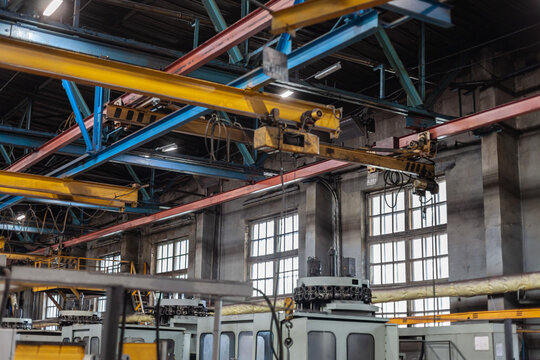 Overhead crane bridge and industrial machinery inside large tractor manufacturing plant. Heavy industry, manufacturing, logistics, mechanical construction, industrial scale, technical infrastructure.