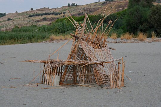 A hut and shelter made of bamboo poles, wooden branches, and fabric on a sandy sea beach. A hand-built hut and beach shelter made of bamboo poles on a sandy coast.