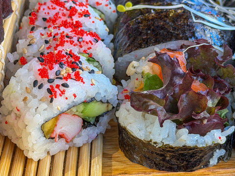 Assorted fresh sushi rolls with tobiko sesame seeds avocado and crab close up on bamboo mat