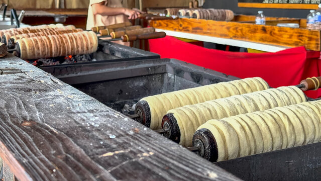 Deinze, Belgium, August 09, 2026 - Traditional trdelnik chimney cakes roasting on wooden spits over open charcoal fire at a food market stall in Deinze, Belgi&euml;