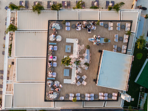 Aerial view of a modern beach club terrace featuring comfortable lounge seating, dining tables, and decorative lighting with people relaxing in Ksamil, Vlore County, Albania.