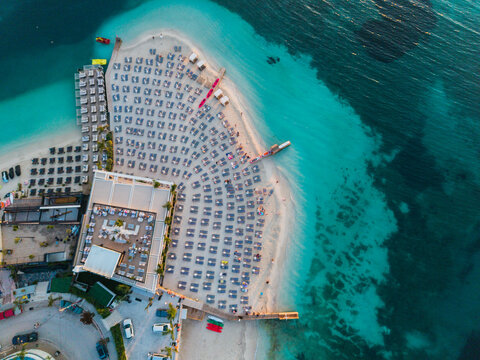 Aerial view of a beach with rows of sun loungers and umbrellas arranged on the sand next to a resort building and turquoise sea in Ksamil, Vlore County, Albania.