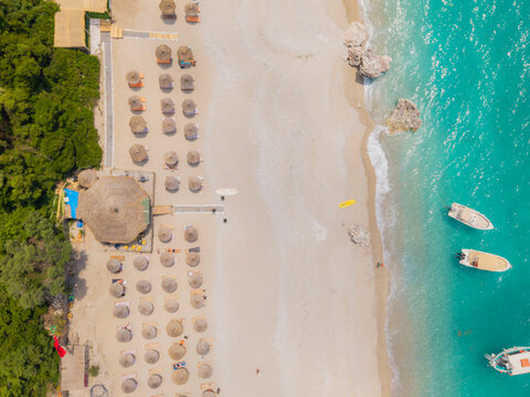 Aerial view of Kroreza Beach featuring rows of sun umbrellas on the sandy shore, turquoise water, and small boats anchored near the coastline in Sarande, Vlore County, Albania.