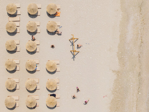 Aerial view of Kroreza Beach with rows of straw umbrellas, sun loungers, and people relaxing on the sand in Sarande, Vlore County, Albania.