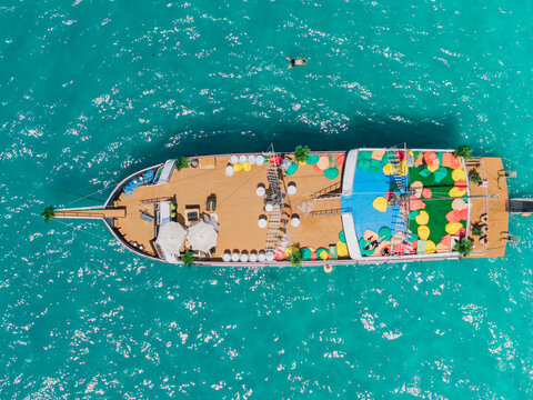 Aerial view of a tour boat with colorful beanbags on deck floating in the turquoise waters of Kroreza Beach in Sarande, Vlore County, Albania.