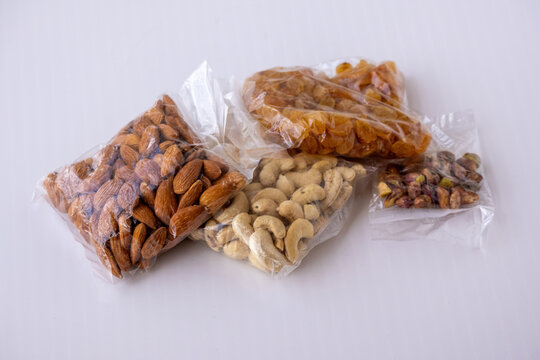 Assorted dry fruits packed in transparent plastic pouches placed on white background. Raw almonds, cashews, raisins, and pistachios packaged for healthy snacks.
