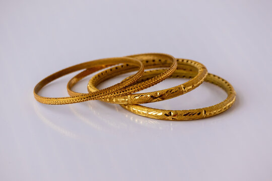 Traditional gold bangles with intricate carved designs placed on white background. Elegant golden jewelry set crafted for bridal wear and wedding ornament.