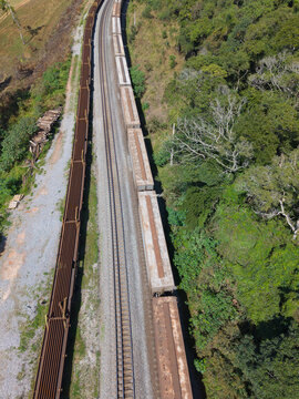 Aerial view of cargo trains moving along railway tracks through a lush green forest in Cotia, State of Sao Paulo, Brazil.
