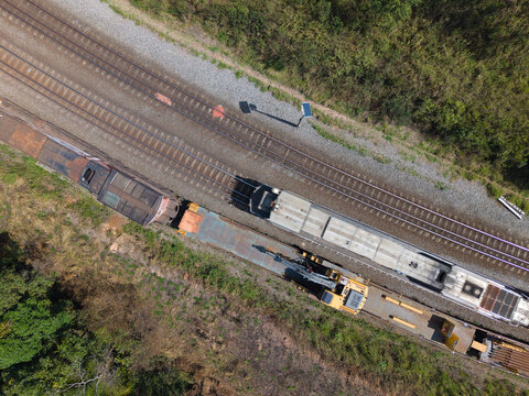 Aerial view of cargo trains on parallel tracks with an excavator on a flatbed car, surrounded by green vegetation in Cotia, State of Sao Paulo, Brazil.