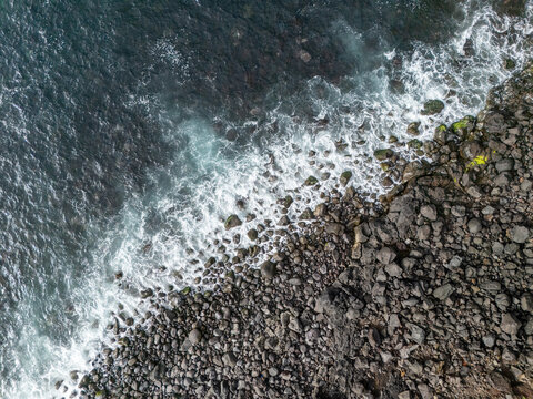 Aerial view of waves crashing against dark volcanic rocks along the coastline, Azores, Portugal.