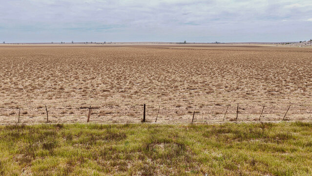 Aerial view of the Karoo landscape featuring vast arid plains, sparse dry vegetation, and a simple wire fence line under a cloudy sky in Beaufort West, Western Cape, South Africa.