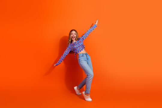 Happy young woman posing energetically against a vibrant orange background wearing stylish casual fashion showcasing laughter