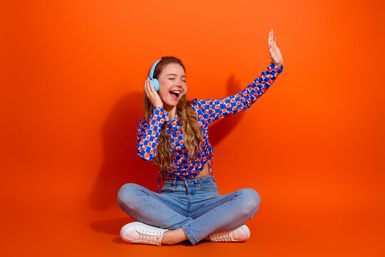 Young Woman with Headphones Enjoying Music Against a Vibrant Orange Background Expressing Joyful Emotions and Relaxation