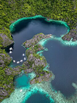 Aerial view of the turquoise waters of Kayangan Lake surrounded by dramatic limestone cliffs and lush tropical vegetation with traditional wooden boats in Coron, Mimaropa, Philippines.