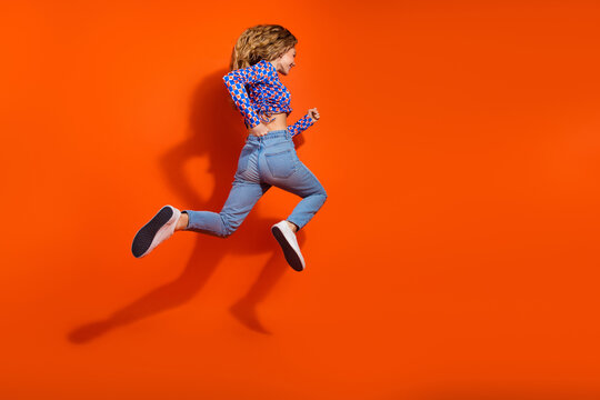 Energetic young woman in casual wear jumping joyfully against a vibrant orange background showcasing modern style