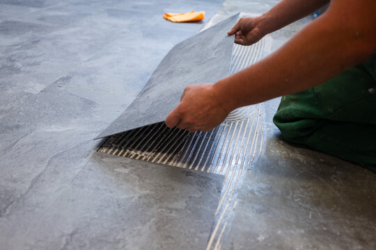 Installer positioning glue-down vinyl flooring panel over adhesive during professional floor installation, illustrating precision craftsmanship in modern interior renovation.