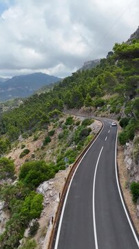 Aerial video of a scenic road winding through mountainous coastal terrain in Mallorca, Spain, surrounded by rocky cliffs, Mediterranean vegetation and dramatic sea views, 4k.