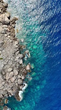 Aerial video looking down on rugged coastal cliffs and crystal-clear turquoise Mediterranean waters along the shoreline of Mallorca, Spain, 4k.