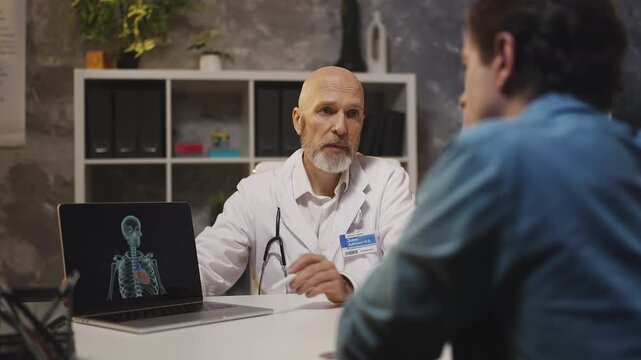 Doctor shows cardiovascular scan on laptop, explaining diagnosis to male patient