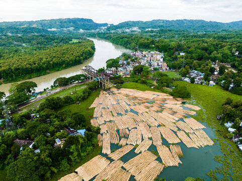 Aerial view of Kaptai Lake with numerous logs floating on the water surface near a town surrounded by lush green hills in Rangamati Hill District, Chittagong Division, Bangladesh.