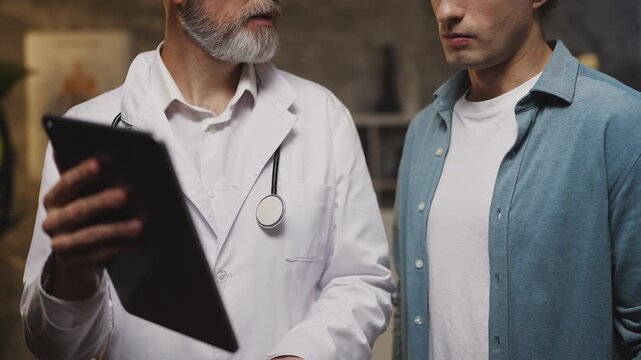 Male physician shows medical test results on tablet to patient during check-up