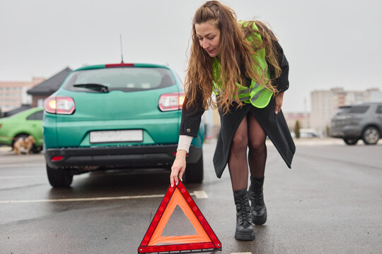 The girl in the green vest is setting up the hazard warning triangle near the car.
