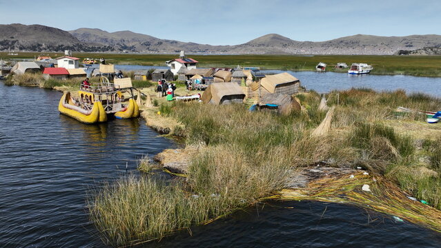 Aerial view of the floating reed islands of the Uros people on Lake Titicaca, featuring traditional thatched houses and reed boats in Urus, Peru.