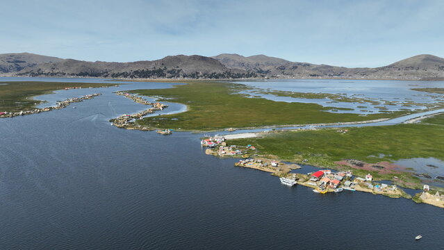 Aerial view of Lake Titicaca featuring the Uros floating islands with traditional reed houses, calm blue waters, and distant mountains under a clear sky in Urus, Peru.