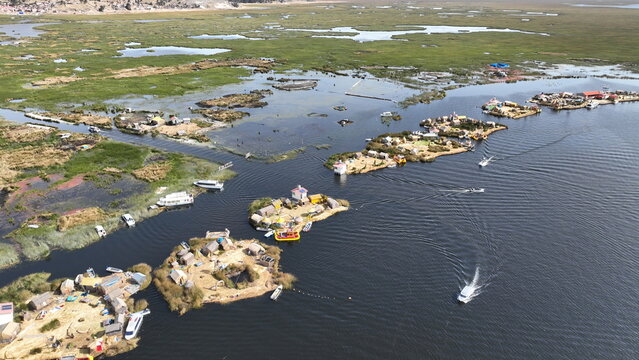 Aerial view of Lake Titicaca with its iconic floating Uros islands made of totora reeds, surrounded by calm blue water and small boats navigating the channels in Urus, Peru.
