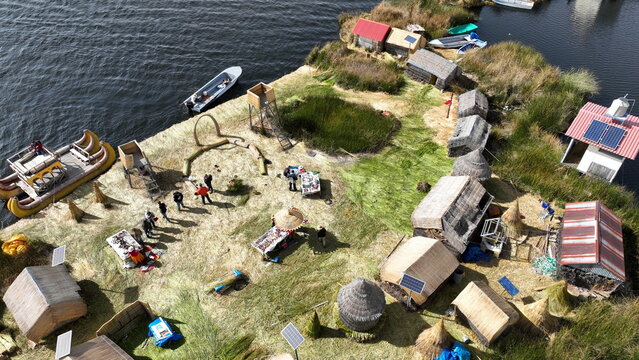 Aerial view of Lake Titicaca and the Uros floating islands, featuring traditional reed houses, solar panels, and boats on the water with people walking around in Uros, Peru.