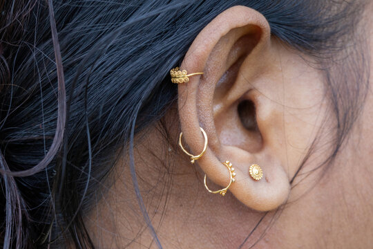 Female ear adorned with multiple traditional golden rings and stud piercings. Ornate gold jewelry worn for traditional beauty and fashion accessory.