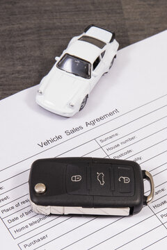 White toy car, car key and form of vehicle sales agreement. Sales or purchases new or used vehicle
