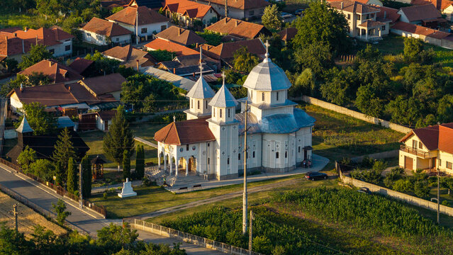Aerial view of a white Orthodox church with silver domes surrounded by residential houses, gardens, and green trees in Deva, Hunedoara, Romania.