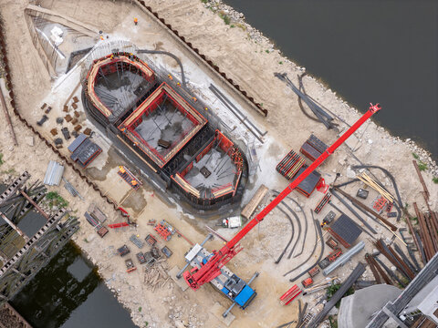 Aerial view of a construction site featuring a red mobile crane, concrete formwork, and workers near the riverbank in Tczew, Poland.