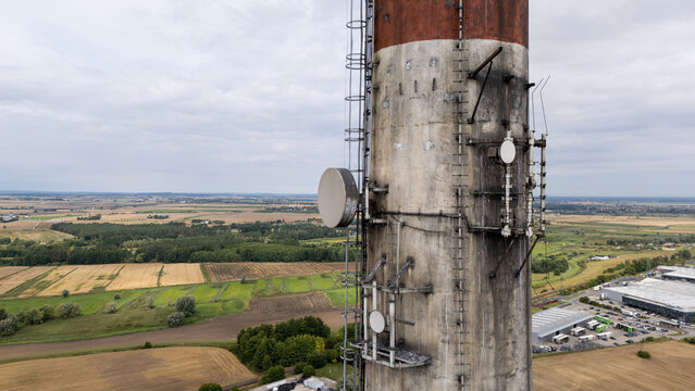 Aerial view of an industrial chimney with communication antennas and satellite dishes rising above the surrounding agricultural fields in Tczew, Poland.