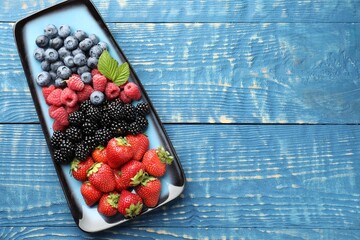 Naklejka premium Different ripe berries and green leaves on blue wooden table, top view. Space for text