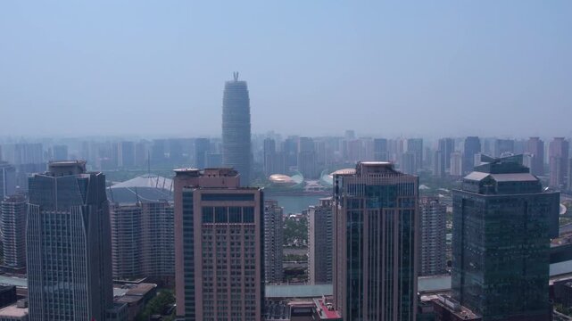 A hazy daytime urban panorama featuring multiple high-rise buildings, a central water body, and a dense city skyline.