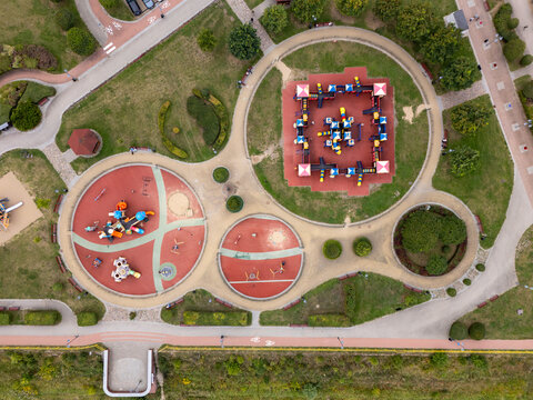 Aerial view of a colorful public playground with circular and square play zones, rubber flooring, and surrounding green park pathways in Tczew, Poland.