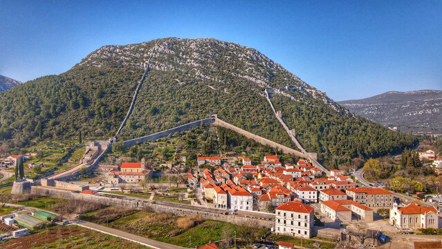 Aerial view of the historic town of Ston and its famous defensive walls climbing the hillside, featuring terracotta rooftops and stone architecture in Ston, Dubrovnik-Neretva County, Croatia.