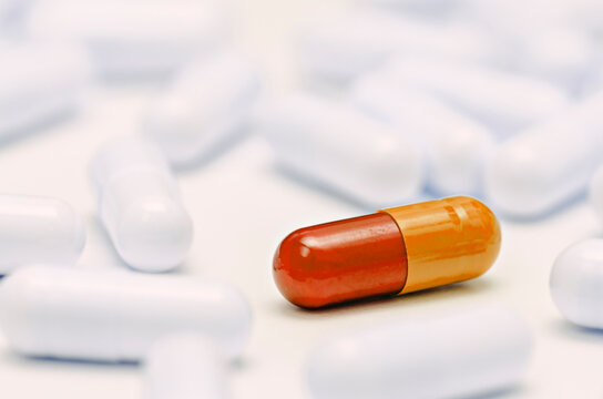 Close up of one orange and red capsule pill standing out among white capsules on a white background