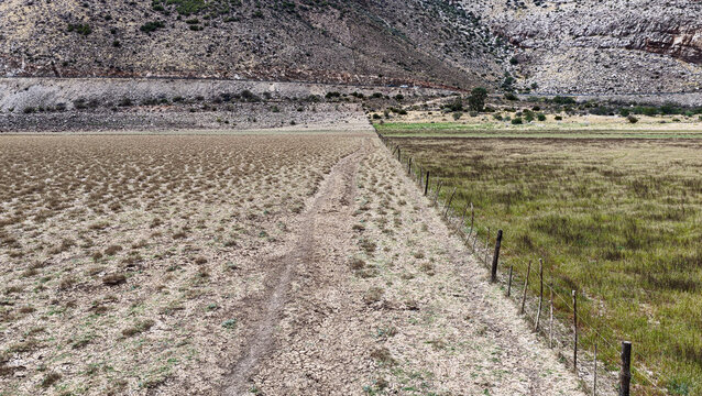 Aerial view of the Karoo landscape showing a contrast between dry arid soil and green vegetation separated by a wire fence with mountains in Beaufort West, Western Cape, South Africa.
